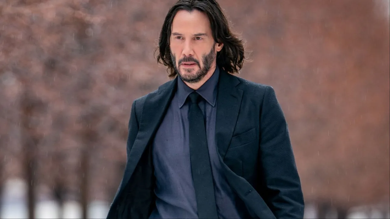 Keanu Reeves como John Wick, em terno preto, segurando uma pistola, ao lado de seu cão, contra fundo urbano