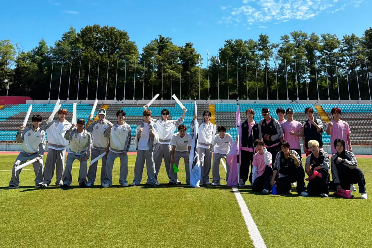 Membros de todas as unidades do NCT em trajes esportivos, posando ao lado de troféus e banner do NCT Athletics Championships
