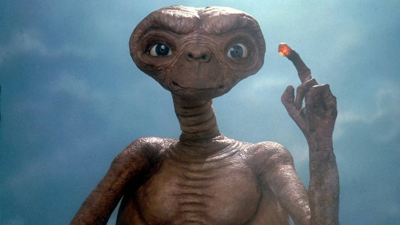 Estante repleta de action figures vintage de Star Wars ao lado de um boneco verde de E.T., ambos sobre caixas lacradas