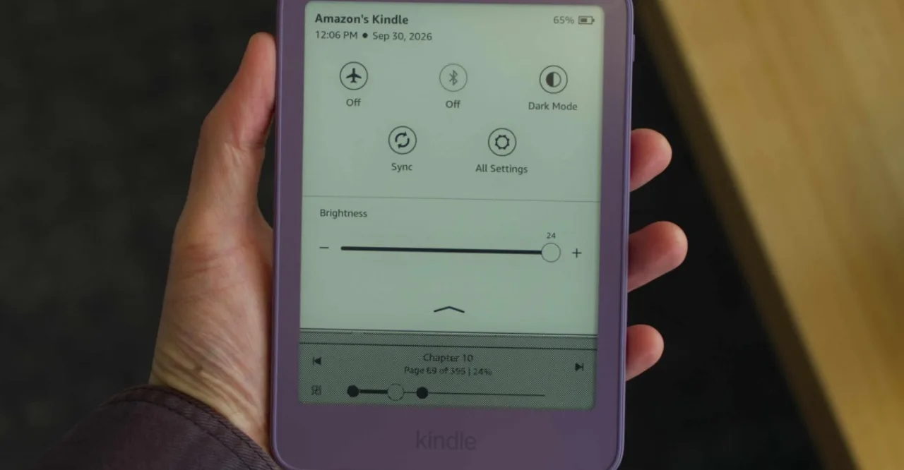 Kindle 2026 com tela escura exibindo manchas de luz nas bordas, segurado por uma mão em ambiente sombrio