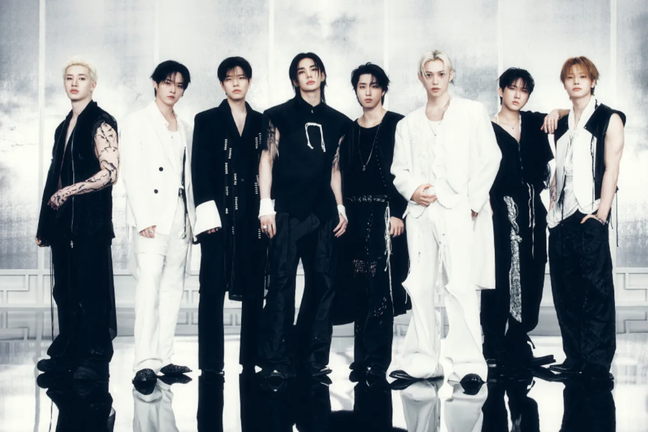 Membros do Stray Kids posam ao lado do troféu Grammy e do logotipo da JYP, com expressão de surpresa
