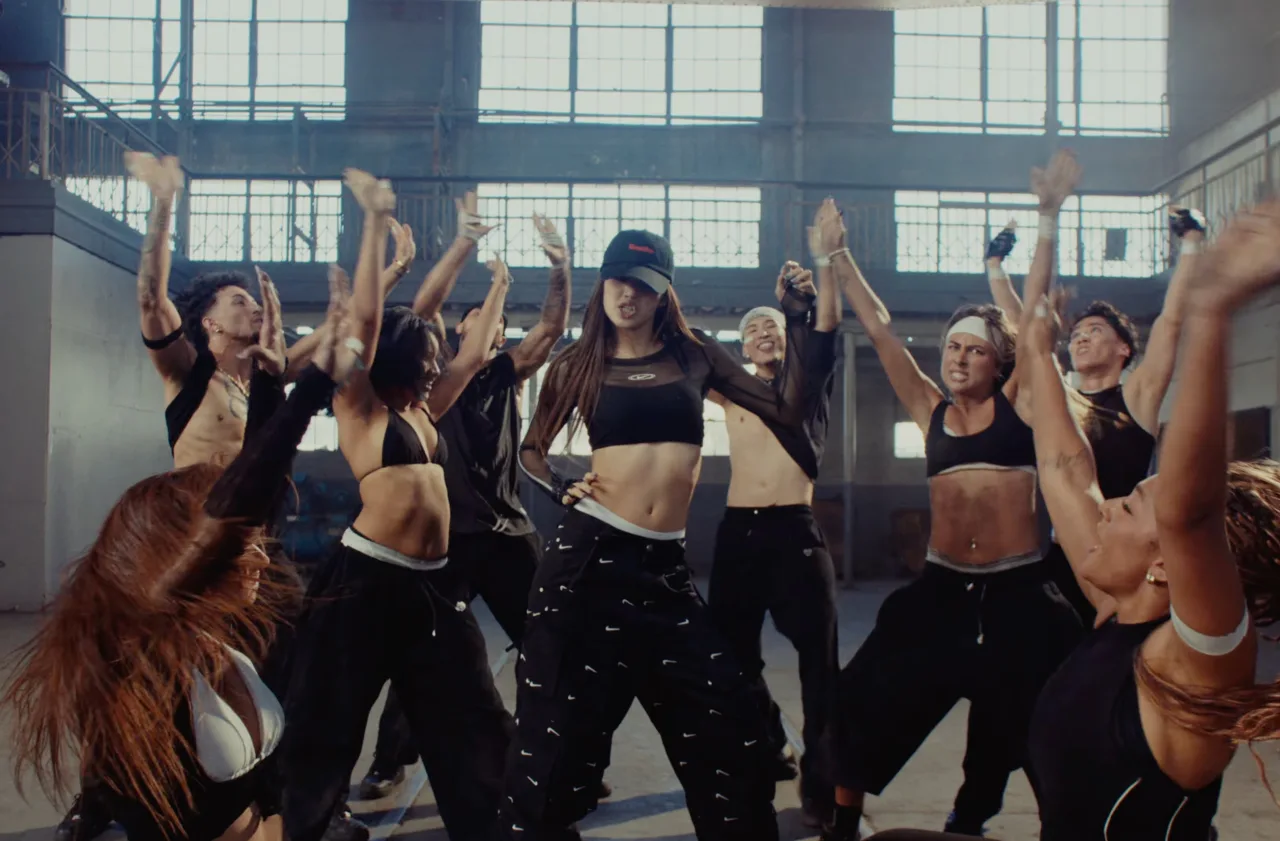 Lisa, de preto, dança “SaWaDiKa” num palco iluminado ao lado de dançarinos de apoio