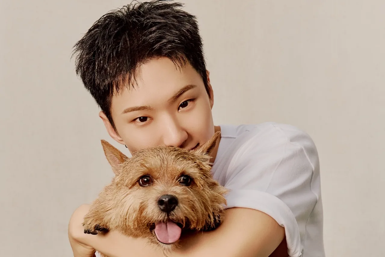 Hoshi, em uniforme militar sul‑coreano, segura a perna com uma tala enquanto exibe o logo do SEVENTEEN