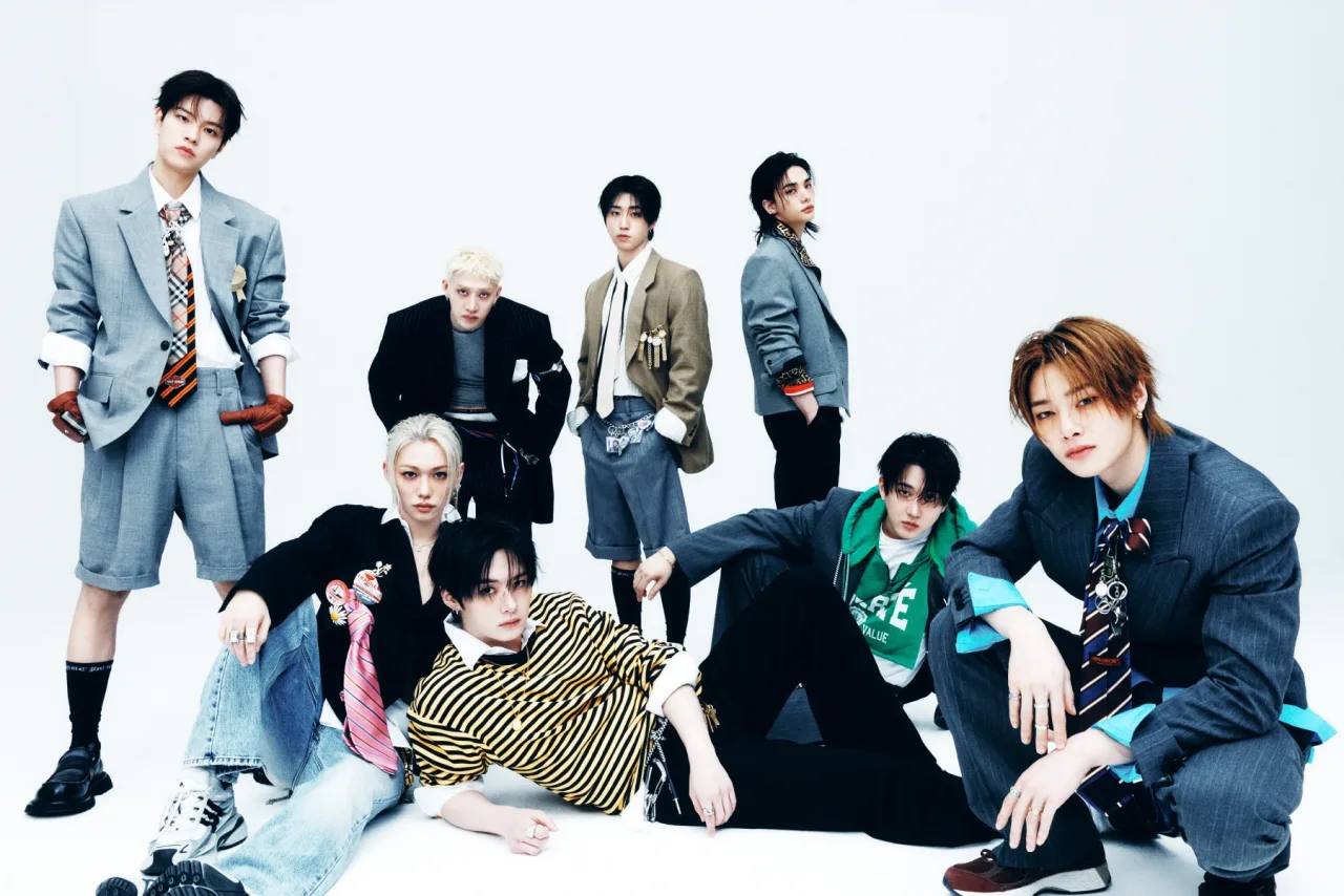 Membros do Stray Kids posam ao lado do disco ‘THIS & THAT’ e da lista da Billboard 200 mostrando a posição 29