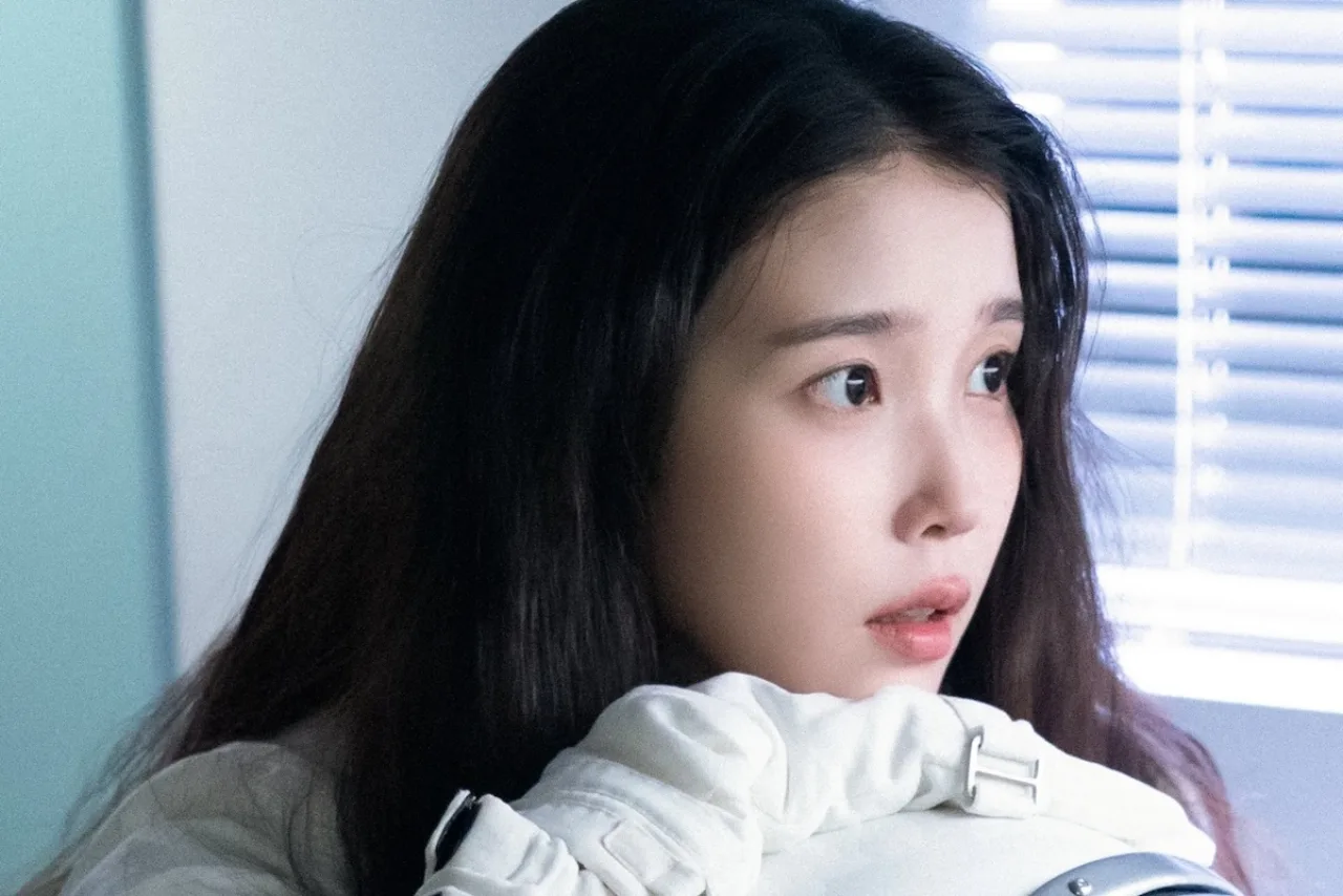 IU aparece sorrindo, vestida de branco, ao lado de um banner que exibe “200 milhões de won” e logos das ONGs
