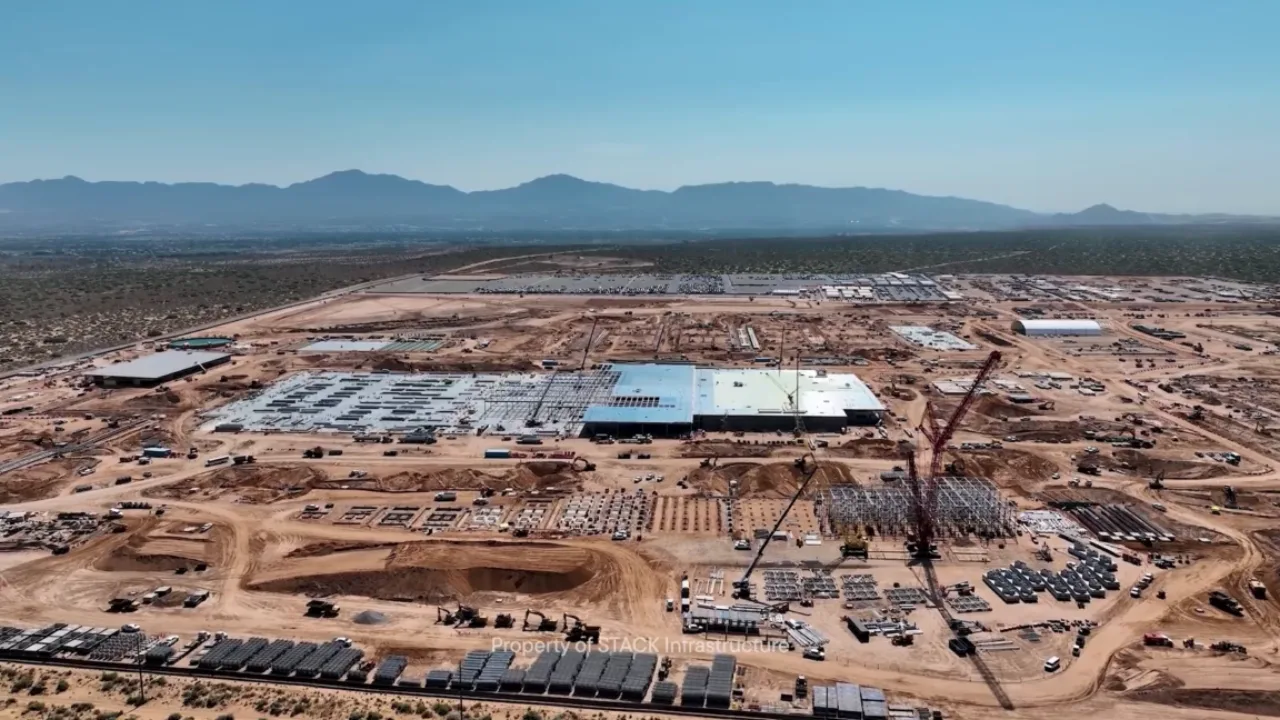Logotipo da Oracle ao lado de turbinas eólicas e painéis solares sobre um data center em paisagem do Novo México