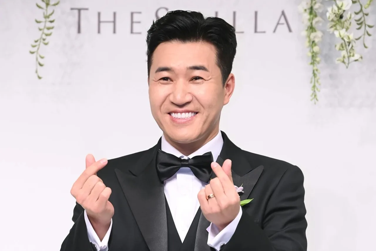 Kim Jong Min abraça a esposa, que exibe a barriga de 17 semanas, diante do letreiro do programa Return Superman