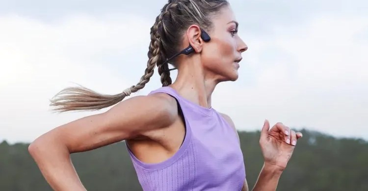 Corredor em pista ao pôr‑do‑sol usando os earbuds Shokz OpenRun Pro de condução óssea, com caixa preta e etiqueta de preço $109